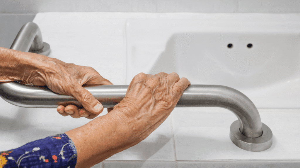 Close-up of hands gripping a stainless steel bathroom safety grab rail next to a sink.