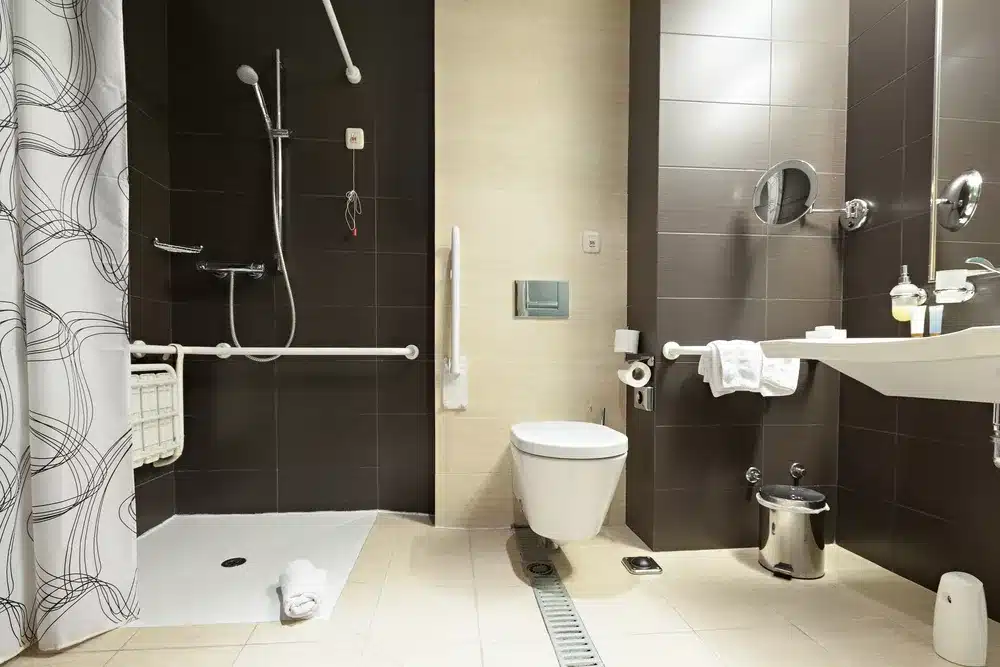 Accessible age care wet room featuring a walk-in shower, grab bars, fold-down seat, toilet with safety rails, sink with wheelchair access, and a range of toiletries and amenities.