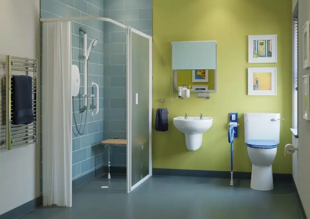 Accessible Age Care Bathroom featuring a walk-in shower, wall-mounted sink, toilet with grab bars, blue and green walls, towel rack, mirror, and framed pictures for a comfortable and stylish wet room environment.