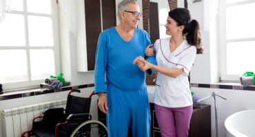 young beautiful nurse helping a senior man holding him by the arm