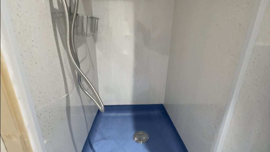 The low-profile, blue anti-slip shower floor in Audrey's wet room, with a corner shower caddy and white sparkle panels.
