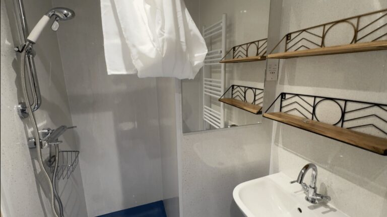 Audrey's finished wet room, with a level shower area, pedestal basin, mirror and decorative wall shelves.