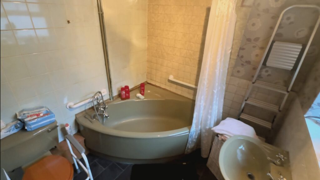 Colin's old bathroom before the work, with a green corner bath, shower curtain and dated tiling