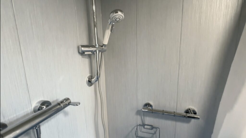 The handheld shower on its riser rail, with a horizontal grab rail and shower basket in Colin's wet room