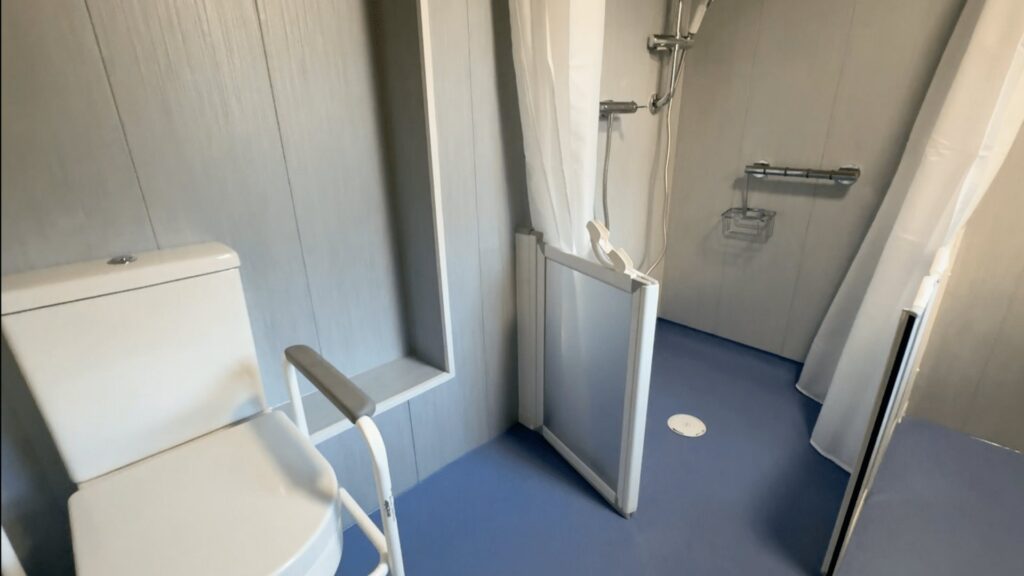 Colin's toilet with support rails beside the level-access shower, with its glass screen and curtain