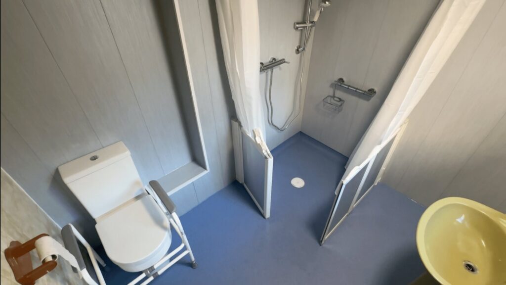 Colin's finished wet room, with a level-access shower area, blue anti-slip flooring, toilet and retained basin.