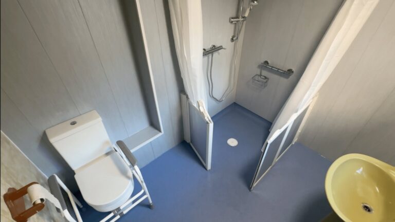 Colin's finished wet room, with a level-access shower area, blue anti-slip flooring, toilet and retained basin.
