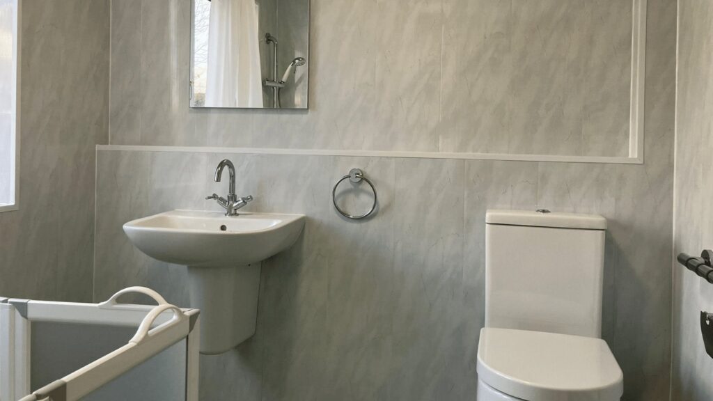 Close-up of Helen's pedestal basin with chrome mixer taps and her comfort-height toilet, against light blue marble-effect panels.