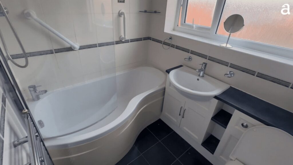 Julie's old bathroom before the work, with a curved bath, over-bath shower screen and added grab rails