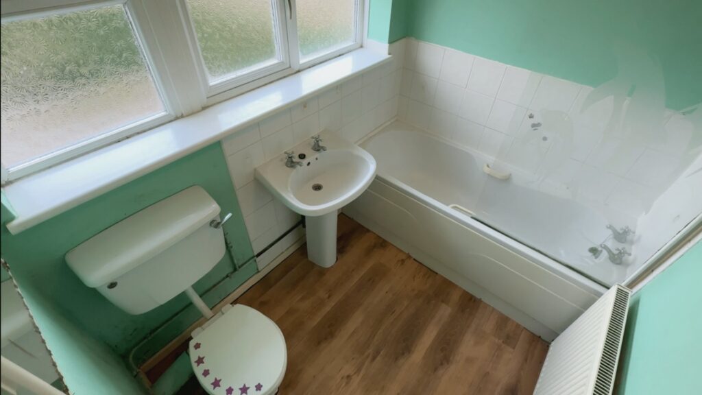 Mark's old bathroom before the work, with a bath, pedestal basin, green walls and wood-effect flooring