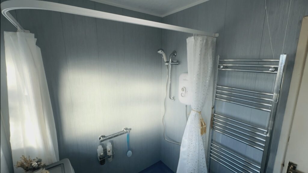 The level-access shower area in Mark's wet room, with an electric shower, riser rail, grab rail and heated towel rail.