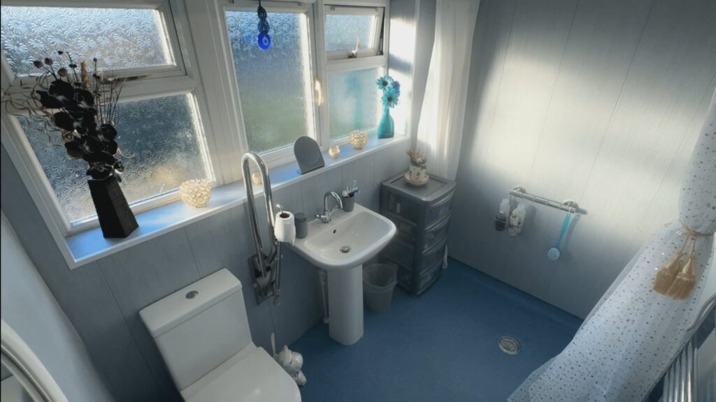 Mark's finished wet room from above, with a level-access shower area, pedestal basin, toilet with a floor-to-ceiling grab pole and blue safety flooring