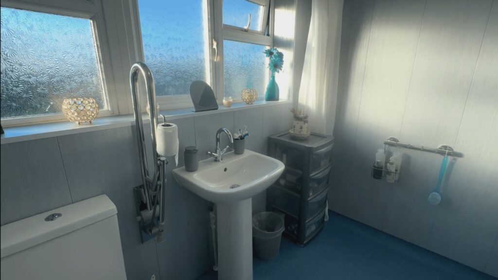 A wide view of Mark's wet room, with light blue wall panels, the shower area behind its curtain and natural light from the window