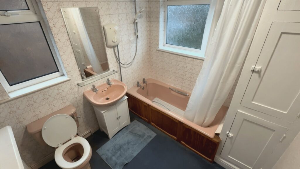 The old bathroom before the work, with a pink suite, bath, over-bath electric shower and curtain.
