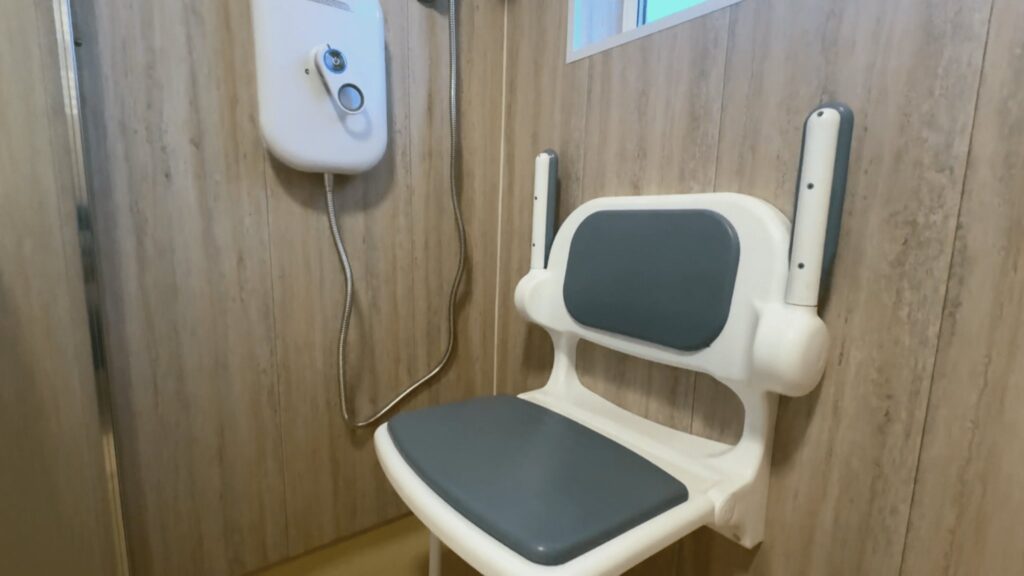 The padded folding shower seat with armrests, mounted on wood-effect waterproof panels.