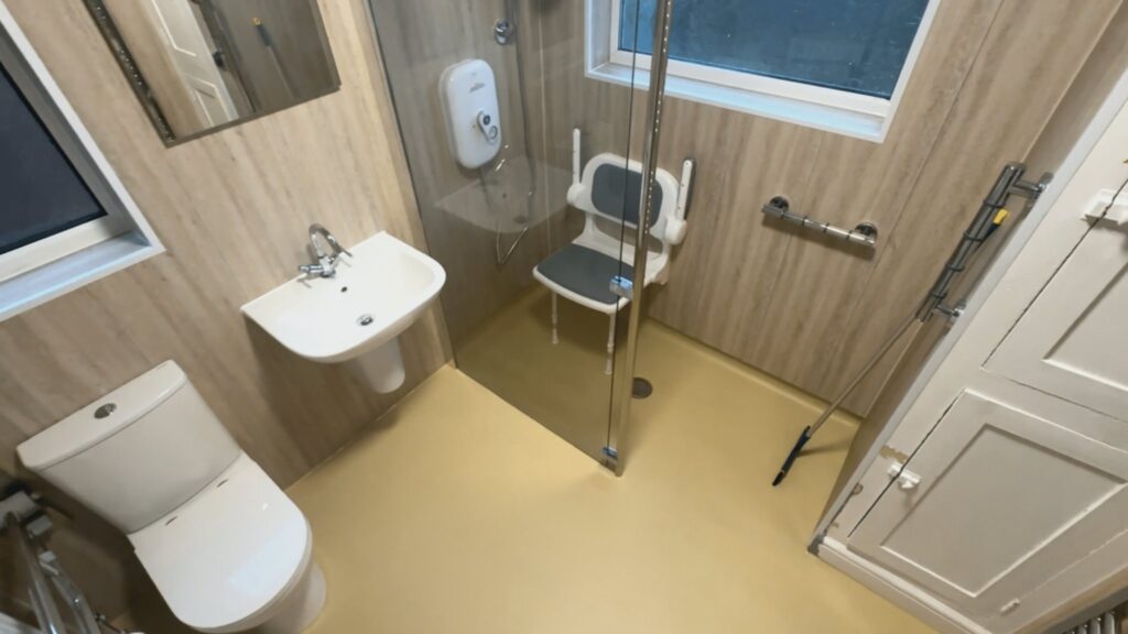 The comfort-height toilet with a folding safety armrest, beside the wall-hung basin