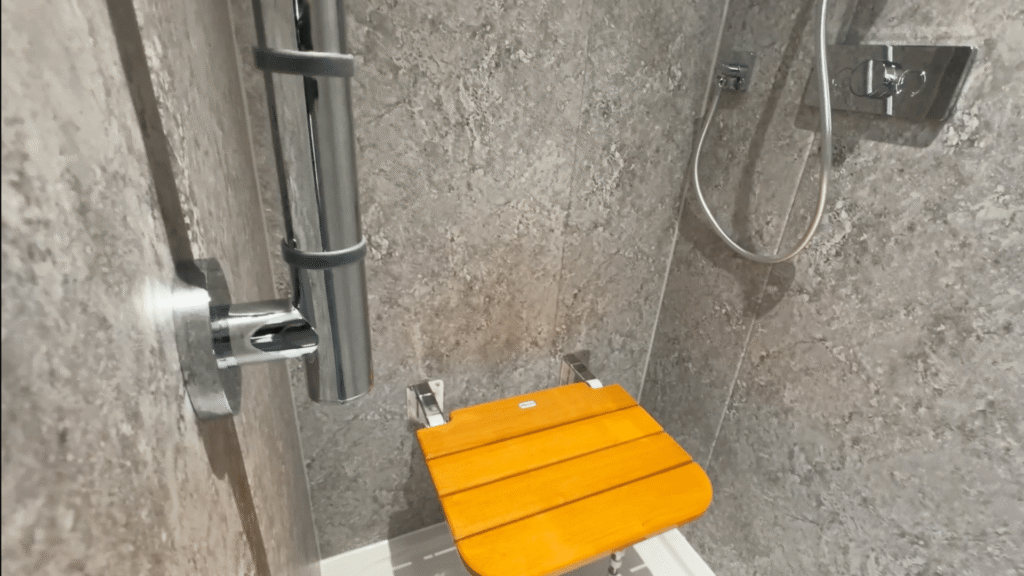 Inside Stephen's walk-in shower, with a fold-down seat and a chrome grab rail.