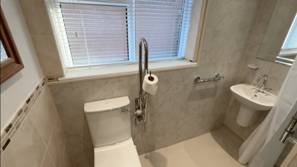 Steve's comfort-height toilet with a hinged support rail and toilet roll holder, beside the level shower area.