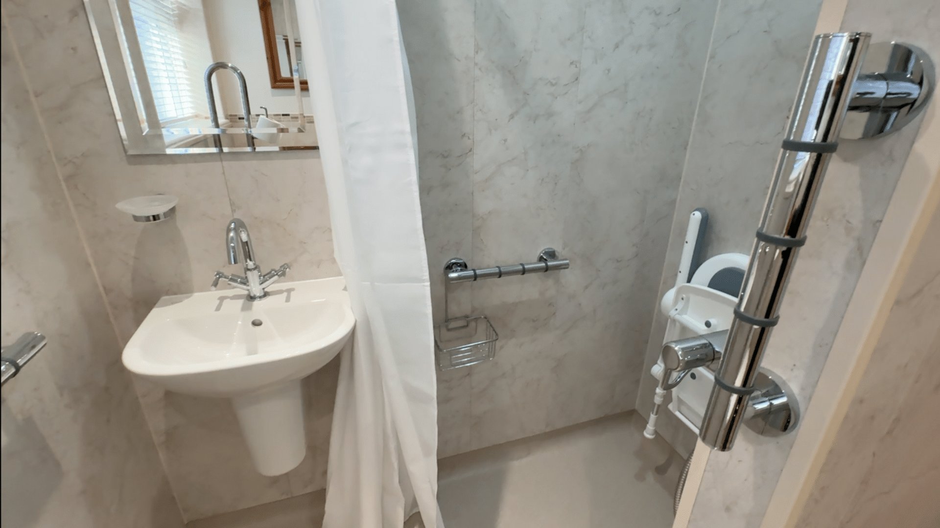 Steve's finished wet room, with a level shower area, folding seat, floor-to-ceiling support pole, grab rail and wall-hung basin.