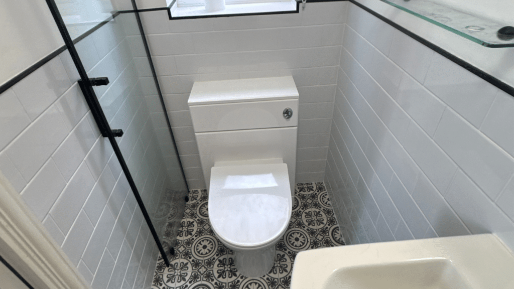 A small, cramped bathroom before renovation by Age Care Bathrooms, featuring white subway wall tiles, patterned floor tiles, and a standard toilet tucked into a tight space.