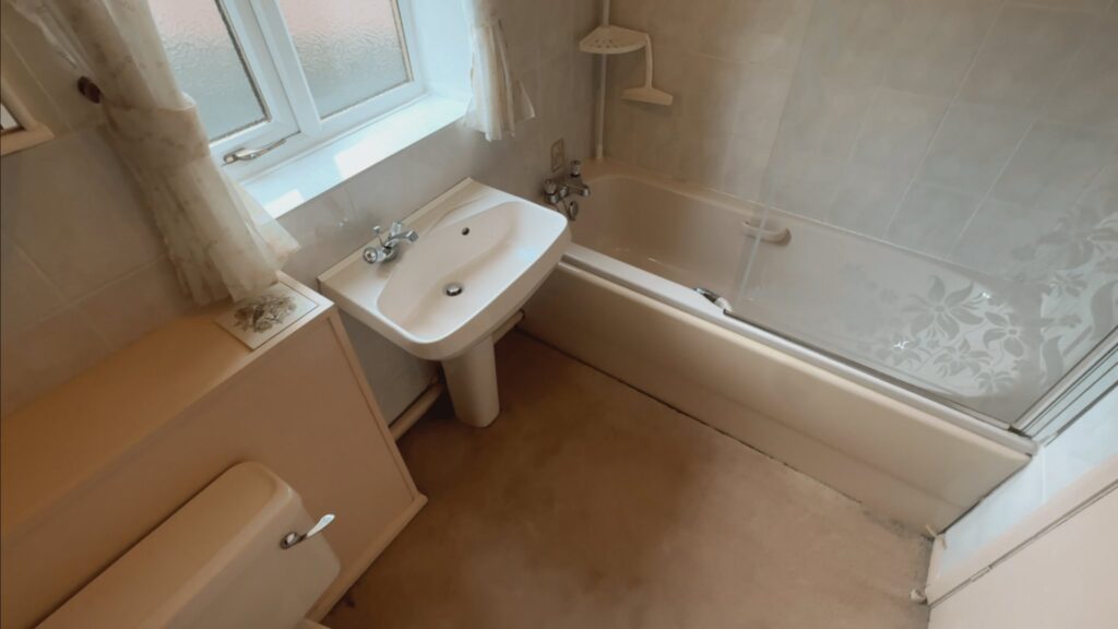 Brian's old bathroom before the work, with a peach bath, over-bath shower screen, pedestal basin and carpeted floor