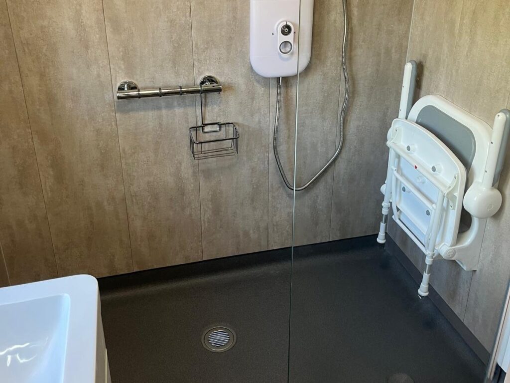 The level shower area in Brian's wet room, with a flush drain, grab rail and glass screen
