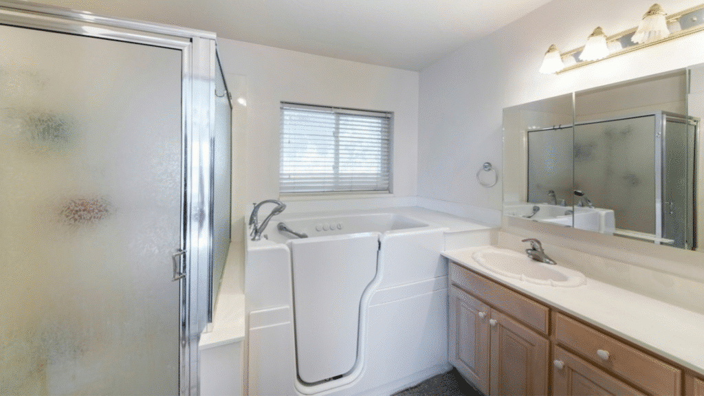 Compact walk-in bathtub with door, installed next to a wooden vanity and glass shower.