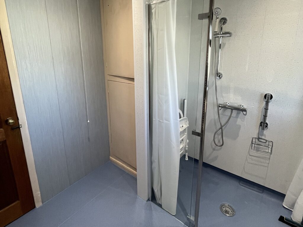 The level-access shower in Bruce's wet room, with a folding seat, thermostatic shower, grab rail and floor-to-ceiling support pole.