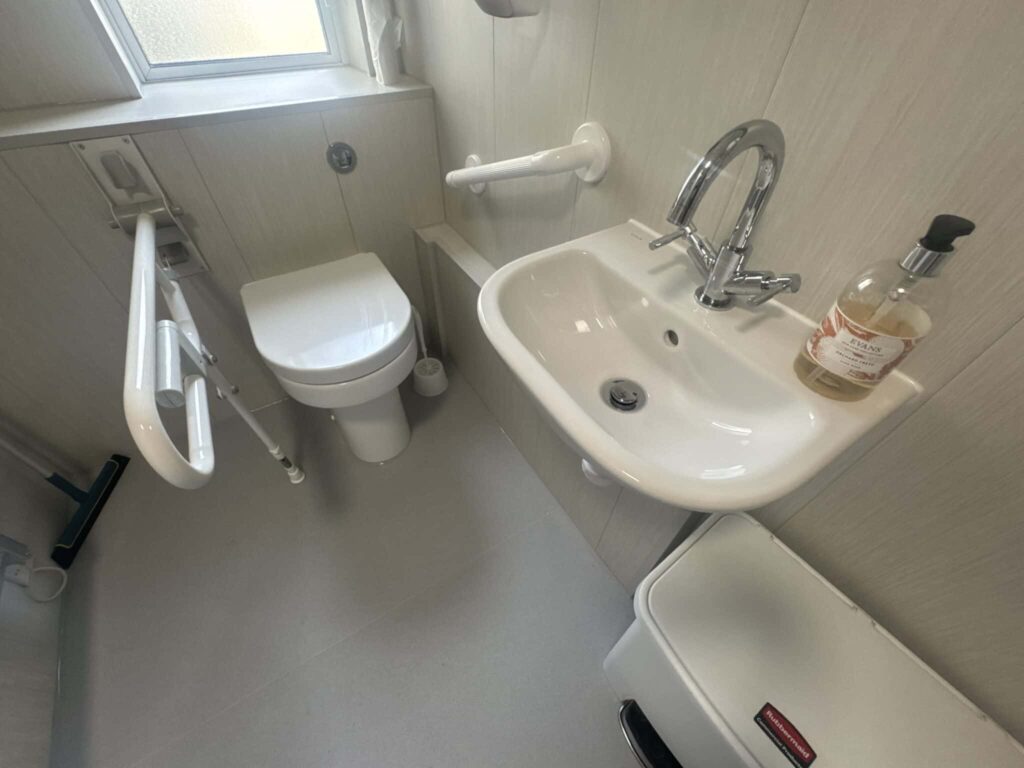 The toilet with a fold-down grab rail and the basin with a fixed safety rail in Room 1.