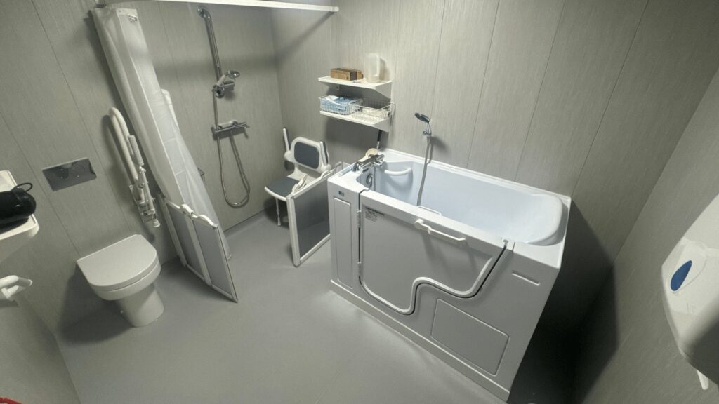 The finished Room 2, with a walk-in bath, folding shower seat, low-profile toilet and light grey waterproof panels