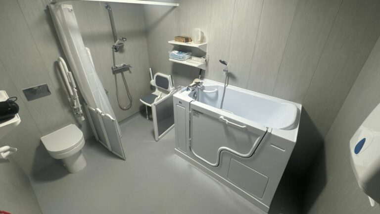 The finished Room 2, with a walk-in bath, folding shower seat, low-profile toilet and light grey waterproof panels