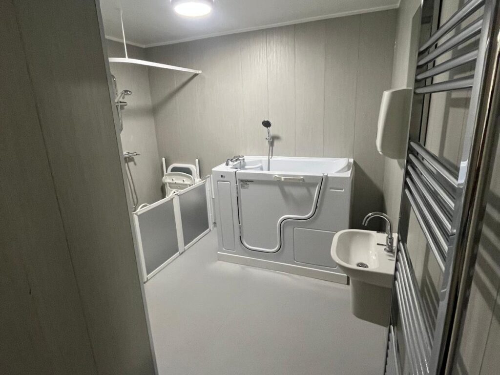 Across Room 2: heated towel rail, basin, walk-in bath and the shower area with its folding seat and half-height doors.