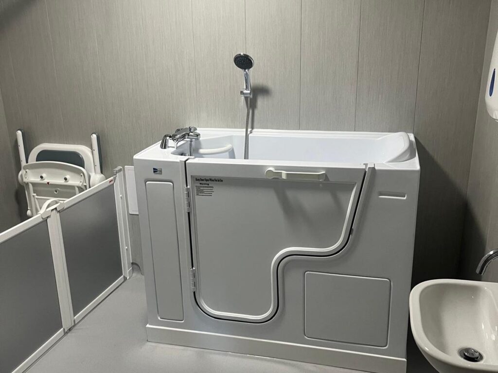 The walk-in bath in Room 2, with a wide outward-opening side door, integrated taps and handheld shower