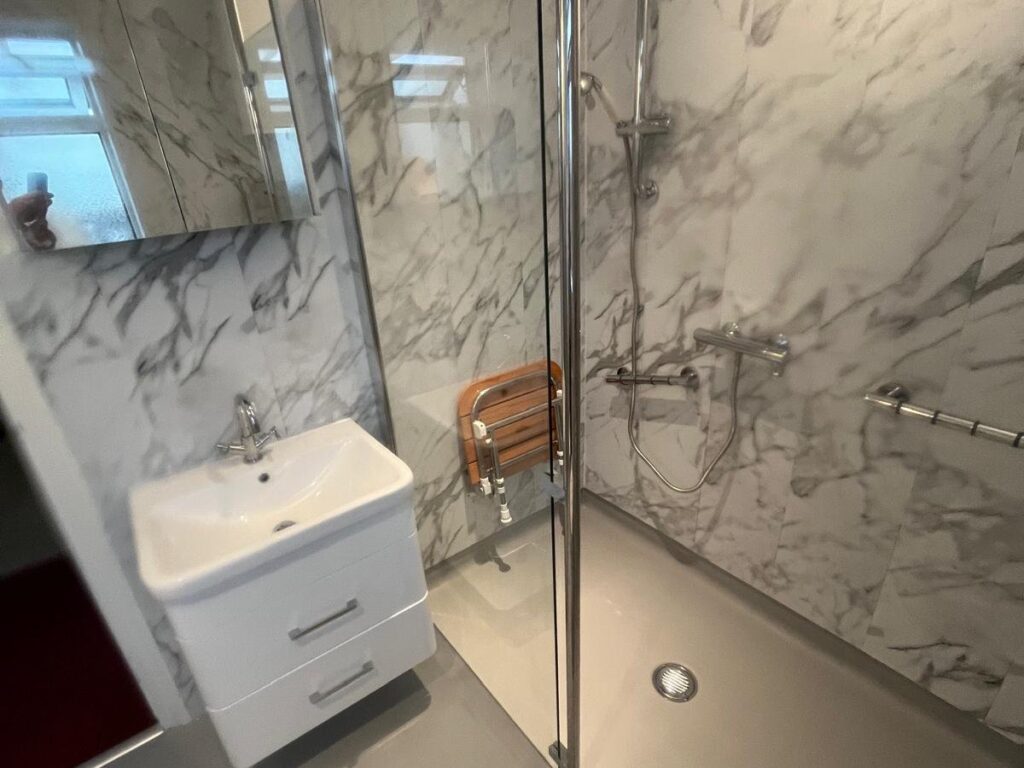 The walk-in shower in Lesley's wet room, with a wooden fold-down seat, grab rails and a riser-rail shower.