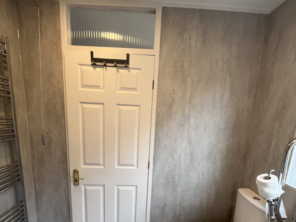 Mark's toilet with a support rail alongside, next to the heated towel rail.
