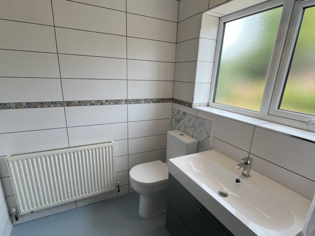 Sandra's comfort-height toilet and grey vanity unit with integrated basin, beside the radiator.