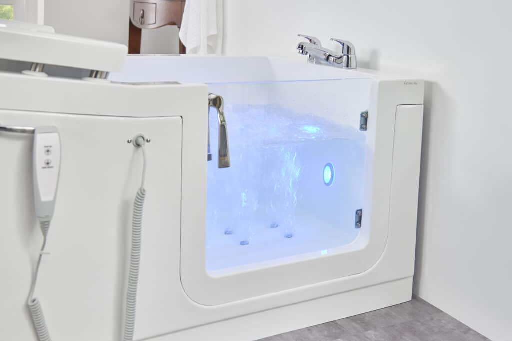 Close-up of a modern walk-in bath with a clear side door, filled with bubbling water illuminated by blue LED lighting.