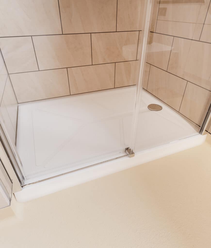Low-level walk-in shower tray with beige tiled walls and a glass screen, designed for easy access.