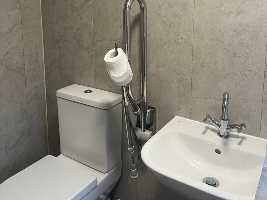 Julie's toilet with a fold-down support rail and easy-reach basin.