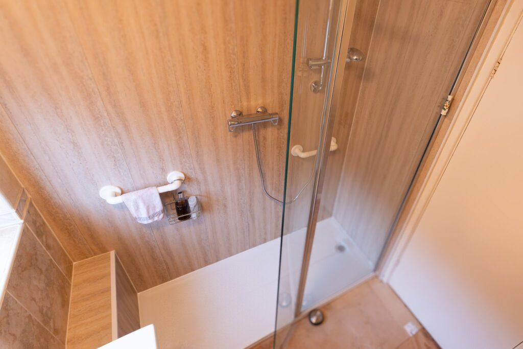Edward's finished walk-in shower, with a glass screen, grab rails, handheld shower-head and level tray.