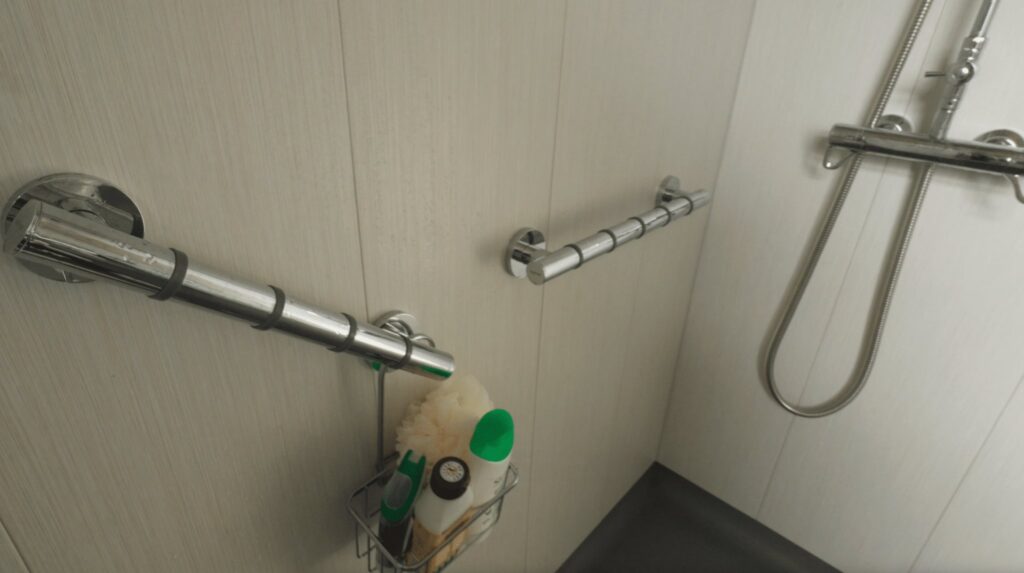 The shower area in Kate's wet room, with two horizontal grab rails, a thermostatic shower and a handheld head.