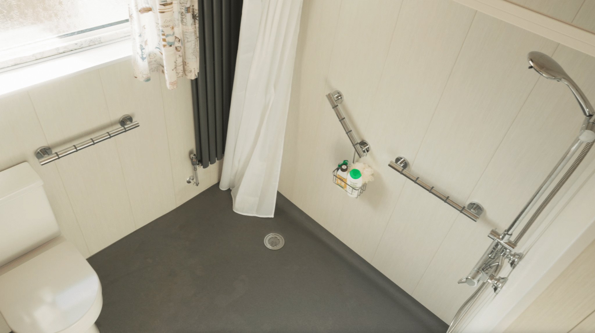Kate's finished level-access wet room: a completely flat floor with a central drain, grab rails on two walls, a thermostatic shower and a toilet.