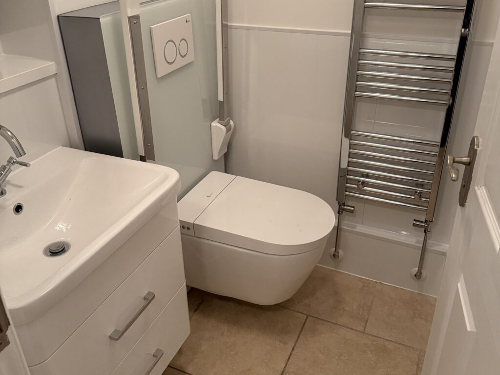 Brent's new rise and fall toilet with its support rails folded away, between the vanity basin and towel rail.