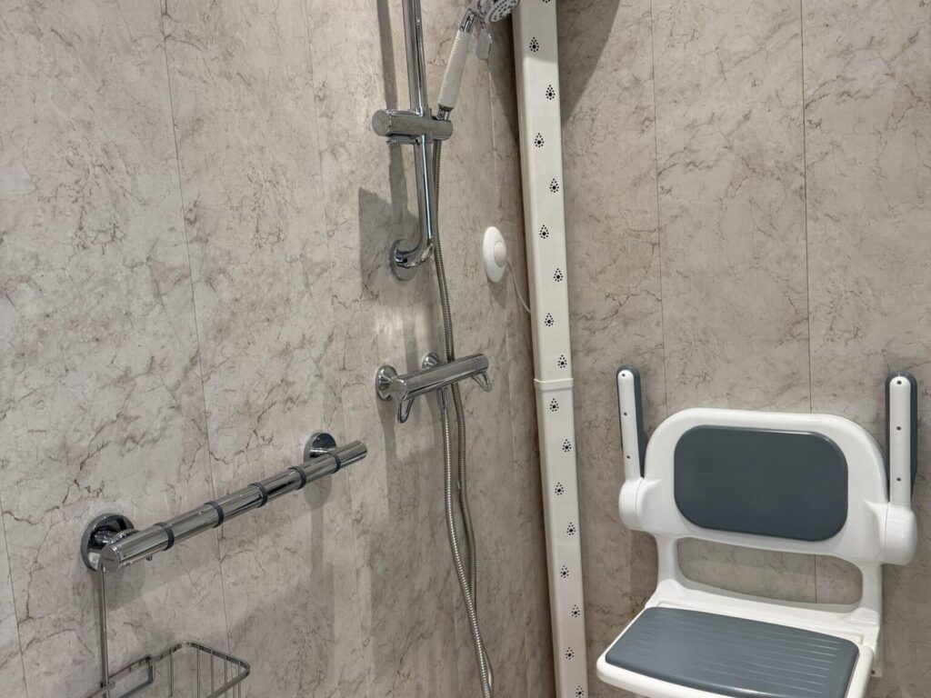 The shower corner in Clare's wet room, showing the thermostatic shower, grab rails, body dryer column and folding seat.