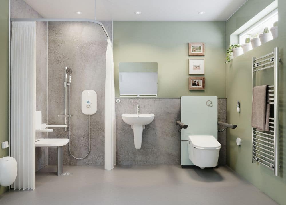 A high-spec accessible wet room featuring an AKW rise and fall bidet toilet system. The wall-hung toilet is mounted on a mint green height-adjustable panel with integrated fold-down armrests. The modern bathroom design includes sage green walls, a level-access shower with a fold-down seat, and a sleek chrome heated towel rail.