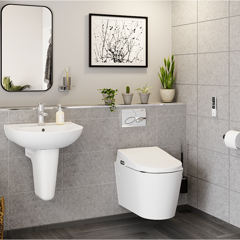 A wide-angle view of a contemporary accessible bathroom featuring an AKW wall-hung bidet toilet, a sleek pedestal wash basin with a minimalist mirror, and neutral grey wall tiles. The design highlights a wall-mounted remote control for the wash and dry functions, providing a practical yet stylish solution for modern mobility needs.