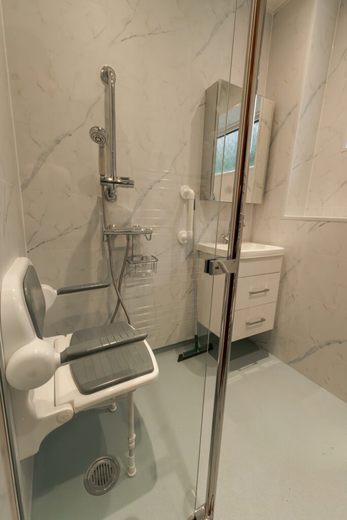 The shower area in Dominic's wet room, with a padded fold-down seat, grab rails and the vanity unit beyond