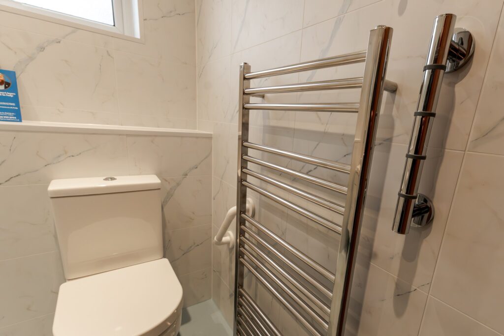 Dominic's new toilet beside the tall heated towel rail, with a grab rail fitted to the marble-effect wall.