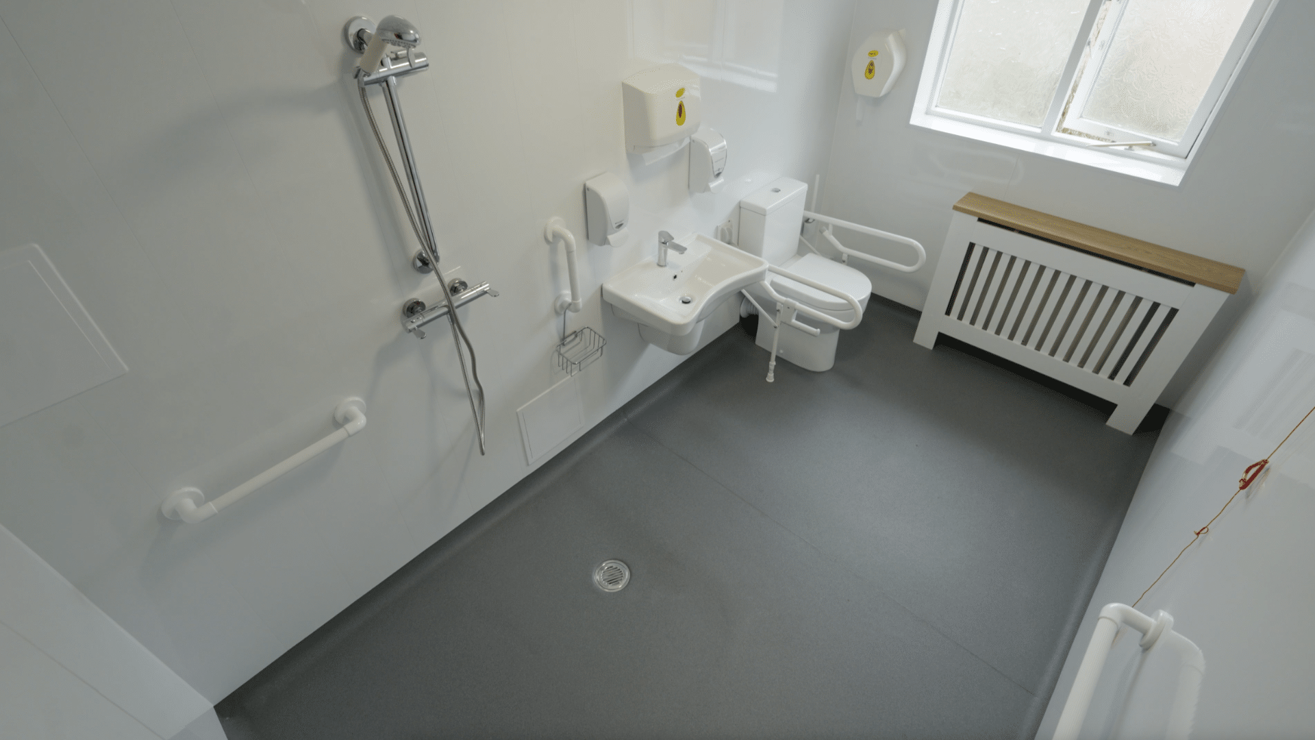 High-angle view of an accessible wet room with a walk-in shower, toilet, and safety grab rails.