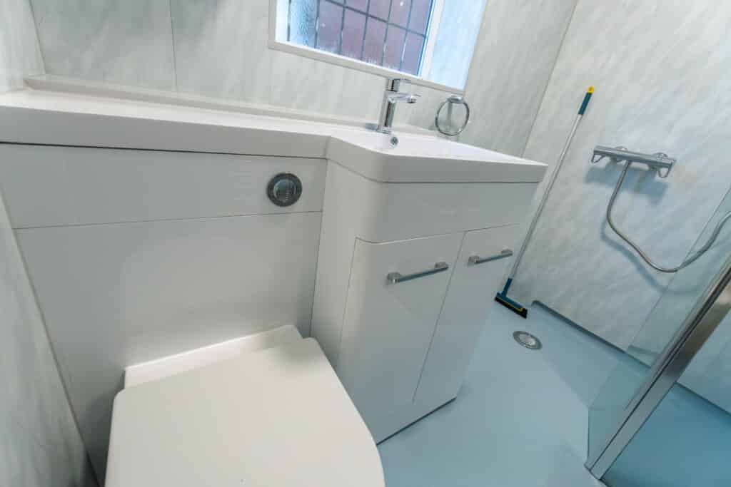 Close-up of a white integrated vanity unit featuring a toilet and washbasin with a chrome lever tap, installed on blue non-slip safety flooring by Age Care Bathrooms as part of an accessible wet room renovation.
